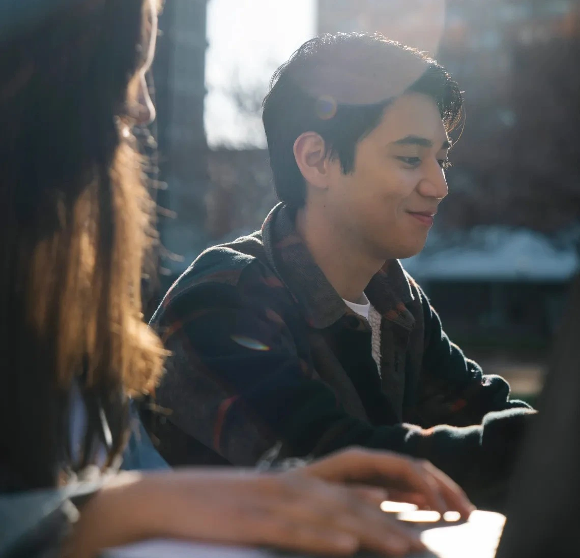 two people sitting at an outdoor table using laptop computers and smiling