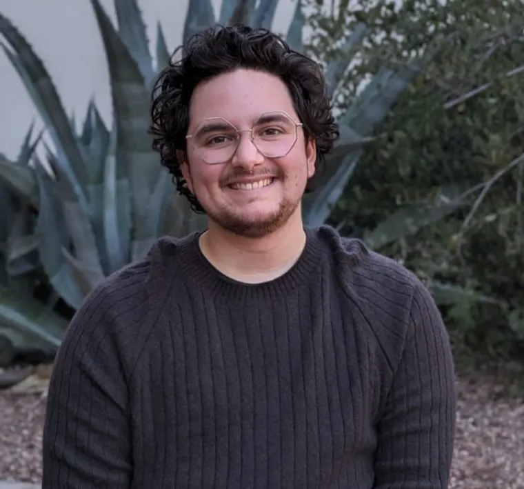 headshot of a person standing outside with grass and trees in the background