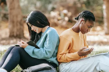 two people sitting back to back wearing earbuds